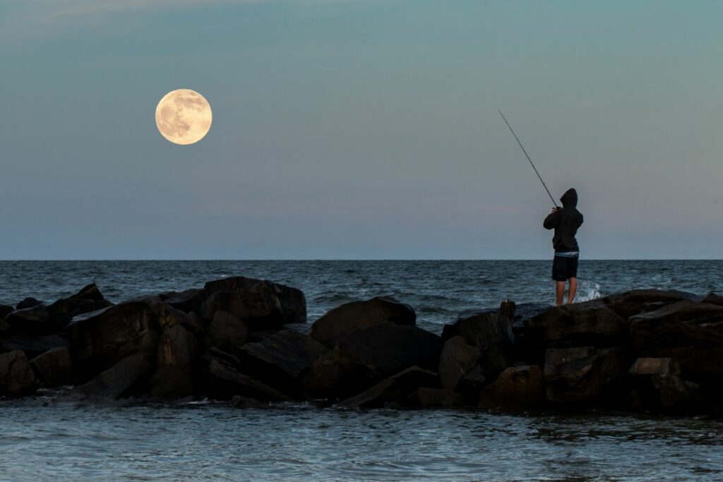 a photo of an angler fishing under the moon to show the best moon phase for saltwater fishing