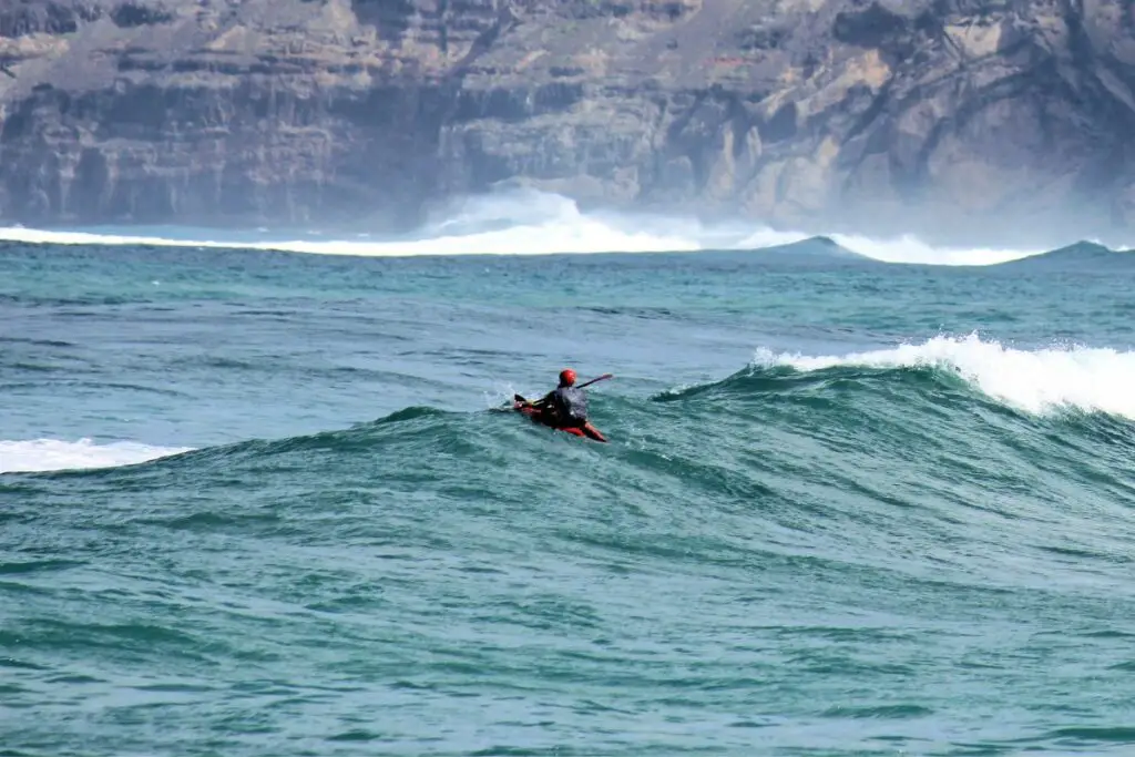 una foto de un kayak en una gran ola para mostrar los peligros del kayak en el océano